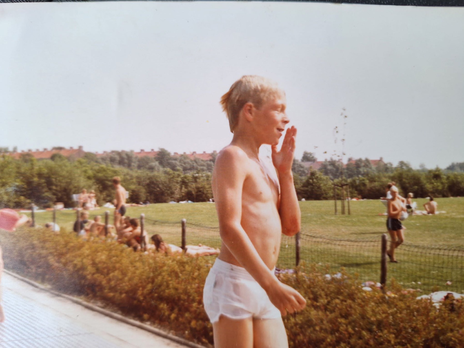 Kleur foto van een jongen bij het openluchtzwembad De Koemen, met bezoekers op het gras op de achtergrond.